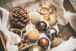 Wooden box of rustic holiday tree decorations, pine cones, baubles, laying on tissue paper, close up
