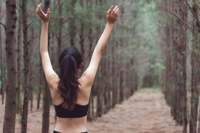 Woman with arms up working out in forest