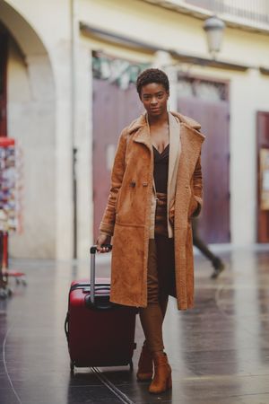 Stylish Black woman with luggage walking on street
