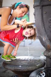 Woman pouring water from fountain for child on street