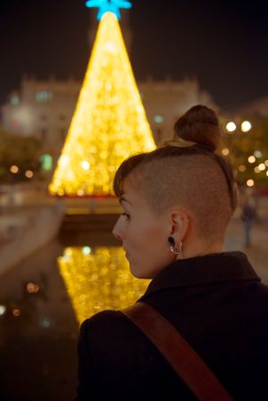 Woman in trendy outfit looking at beautiful shining Christmas tree