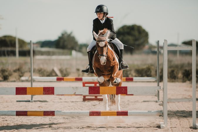 Teen girl riding horse and jumping over bars