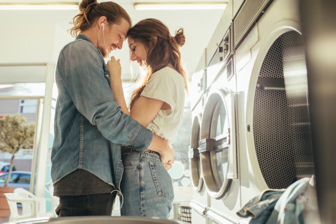 Couple enjoying listening to music sharing earphones standing in a laundry room