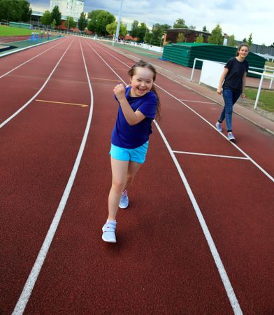 Happy young child running on track with sister in the background