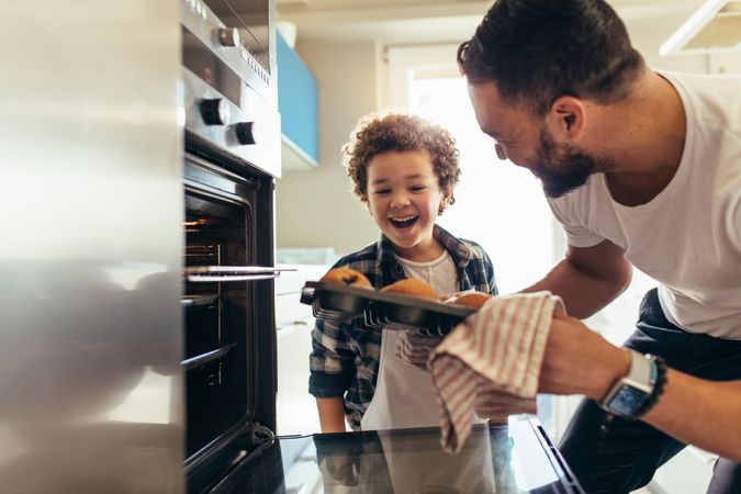Man showing baked cookies to his son while taking them out of the oven