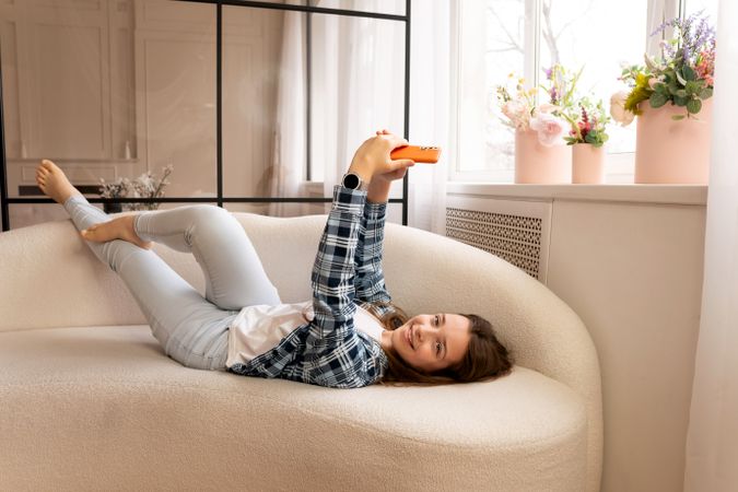 Happy teenage girl lounging on sofa taking cheerful selfies.