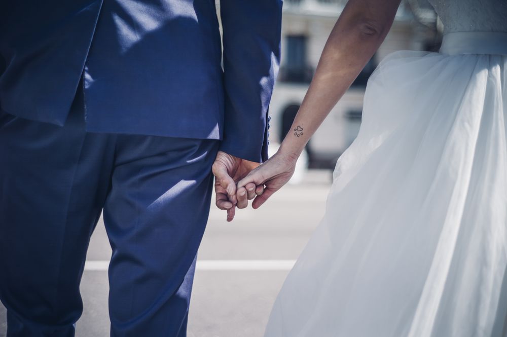 crop man holding on hands woman in wedding dress on street in sunny day