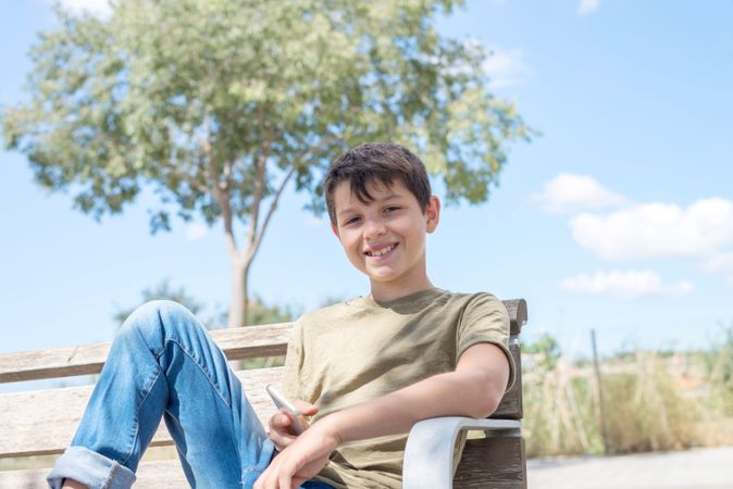 Smiling boy sitting on bench holding phone