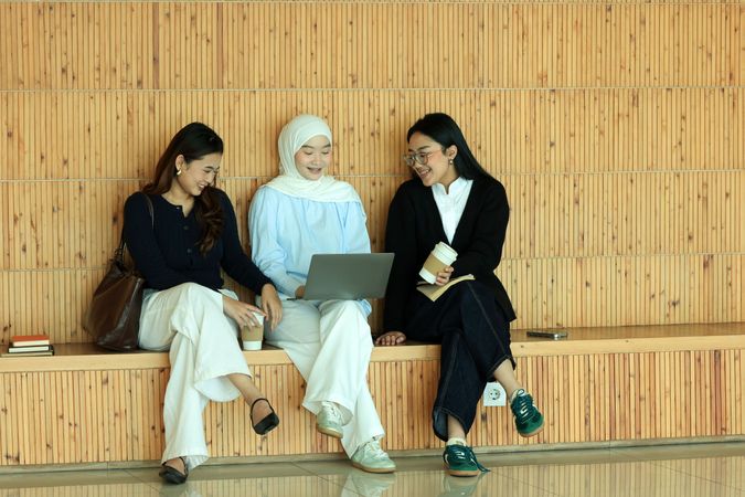 Three Asian University Students Woman Discussing Reading Books Together in  Campus Learning Space using Laptop Computer.