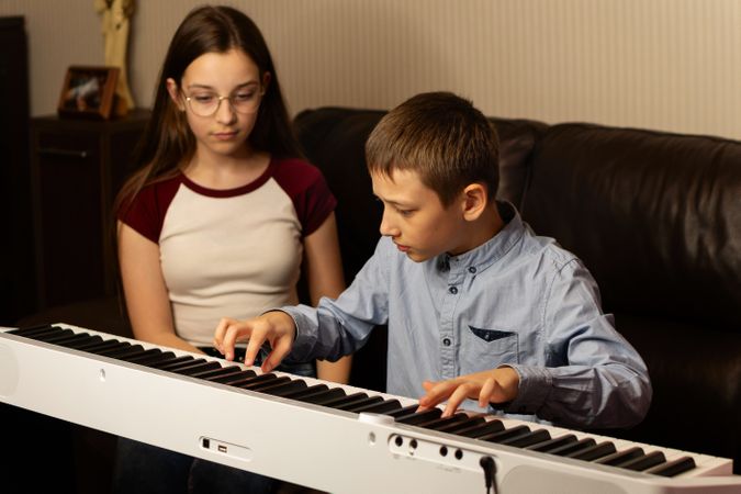 Boy practicing keyboard while girl observes with focus.