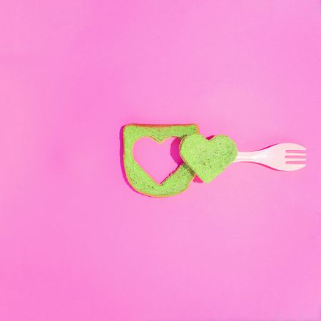 Green toast with heart cut out on a pink background with fork