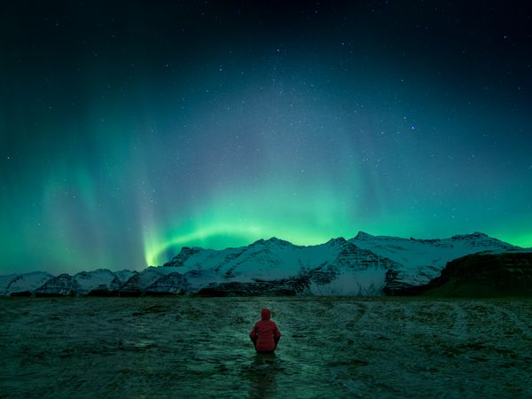 Person wearing red hoodie sitting on floor looking at the northern lights