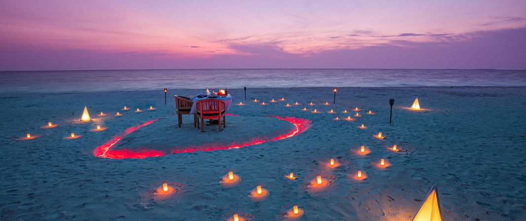 Wide shot of a beautiful dinner setting on a beach with candles at dusk