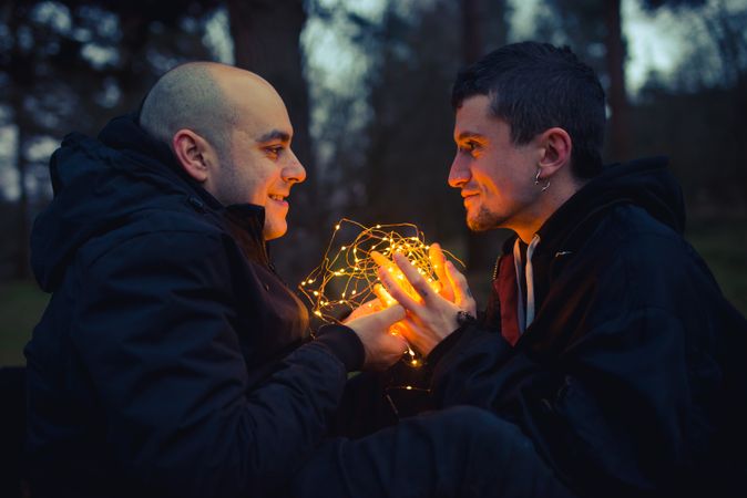 Men holding fairy lights near dog in forest at night