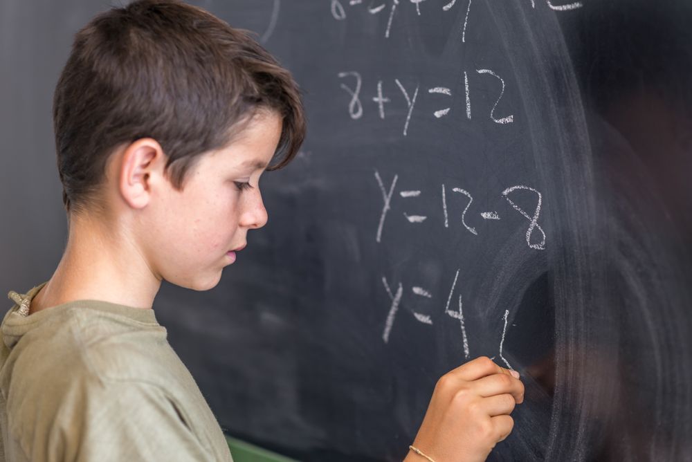 Teenage boy solving equation at chalk board