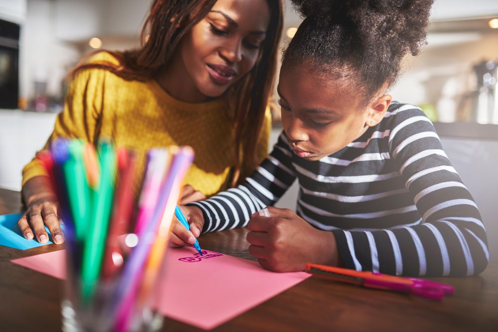 Mother looks over daughter as she draws in the kitchen