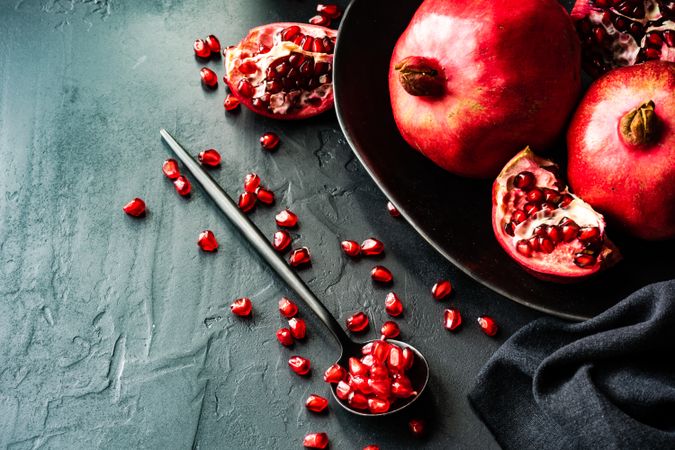 Spoon with pomegranate seeds next to fruit bowl on dark table