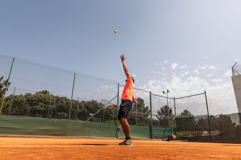 Man in sportswear playing tennis on a dirt tennis court