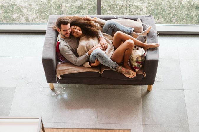Young multiracial couple hugging on sofa