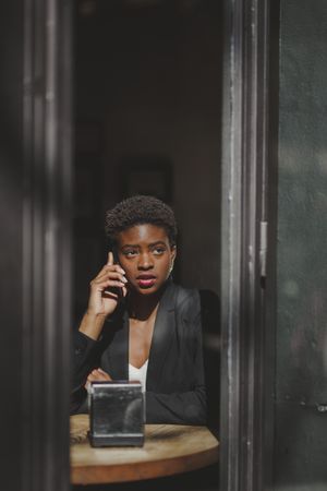 Serious stylish Black woman talking on smartphone in cafe