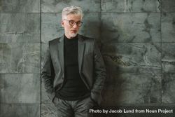 Portrait of handsome mature man in business suit standing on grey wall 5RKN24