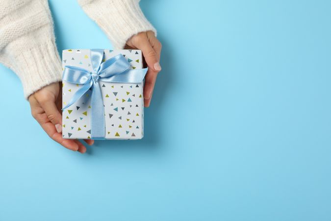 Young woman holding gift box on light blue background, space for text