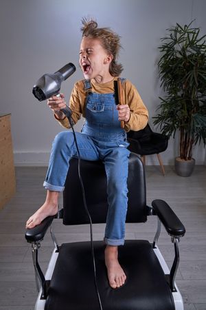 Child in a hairdresser's singing with a hairdryer and a brush
