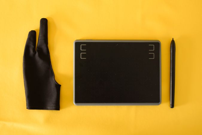 Top view of digital tablet, glove and stylus on yellow table