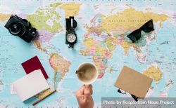 Person holding a cup of coffee over the world map with camera and compass over it 5zPKnb