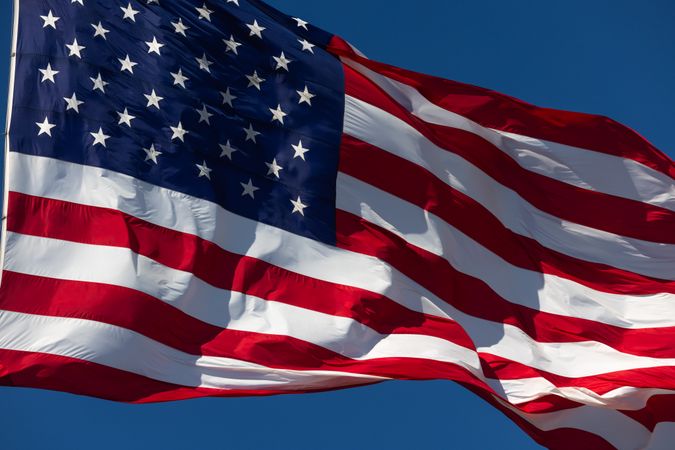 American Flag Waving In The Wind Against Deep Blue Sky.