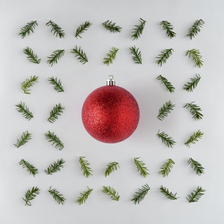 Red holiday decorations surrounded with branches arranged around it on light background