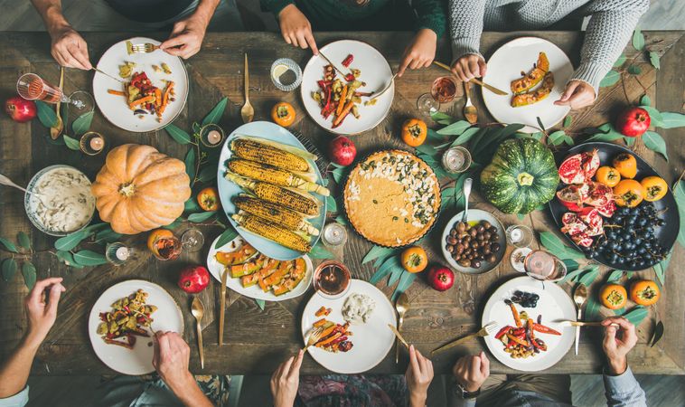 Group of people over festive vegetarian table setting with pie and corn
