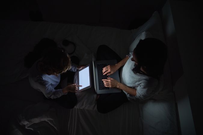 Mother with son browsing gadgets while doing homework in darknes