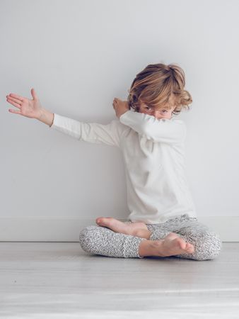 Boy in white pajamas leaning against the white wall of his house.