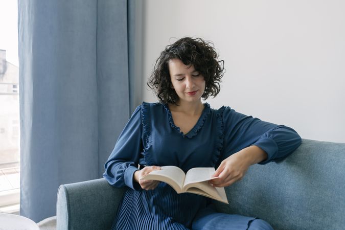 Young female reading book sitting on sofa