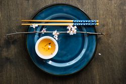 Top view of table setting with chop sticks on ceramic navy plate and delicate cherry blossom branch and cup of tea