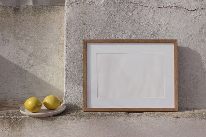 Blank horizontal wooden picture frame mockup against old textured shabby wall. Fresh yellow lemons fruit. Summer background. Mediterranean still life, design. Artistic poster mock-up.