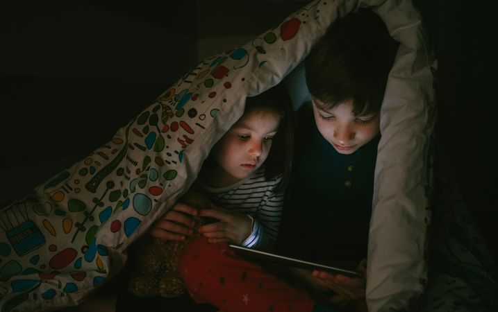 Siblings looking at the tablet in the dark