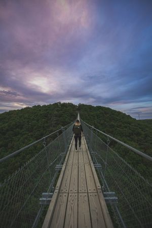 Back of woman walking on suspension bridge in mountain