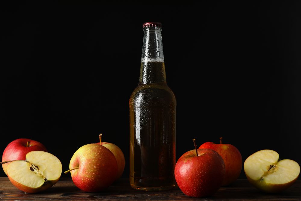 Composition with cider and apples on wooden table against dark background