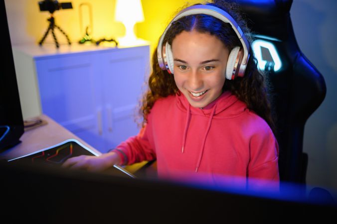 Top view happy teenage girl in headphones sitting at table and playing games in room