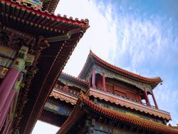 Two traditional Chinese buildings with red and gold accents, showcasing intricate designs, set against a blue sky with soft, scattered clouds