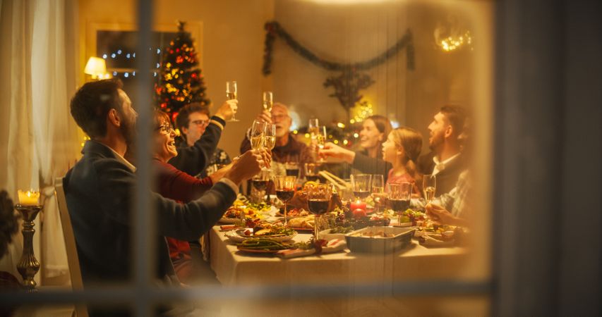 Cinematic Shot Through a Snowy House Window: Christmas Dinner Together with Parents, Children and Friends at Home.