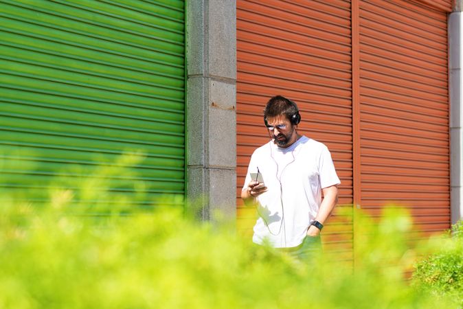 Man checking phone while walking next to colorful shutters