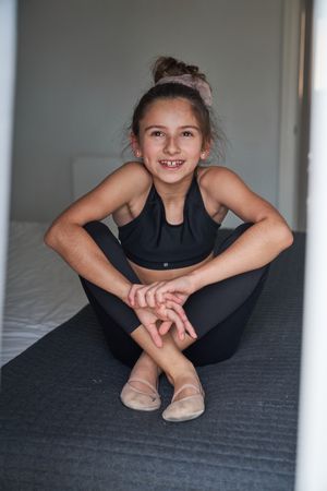 Smiling preteen gymnast in sportswear sitting on bed