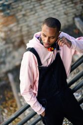 Male in overalls and hoodie leaning on railing of stairs outside