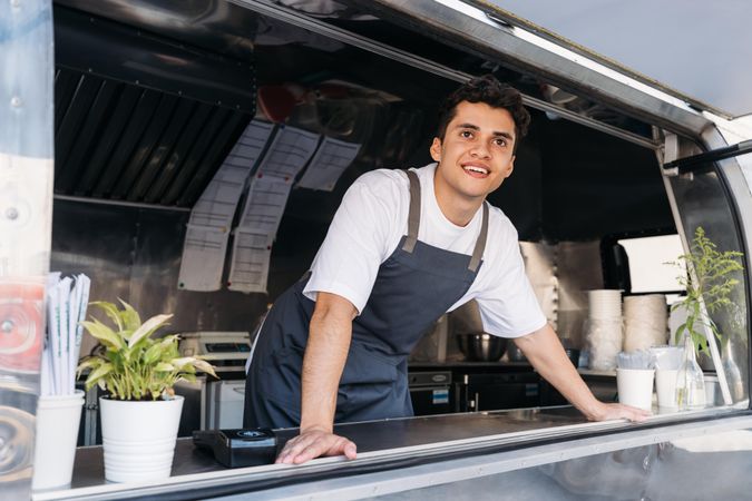 Happy male food truck vendor looking out of van from kitchen