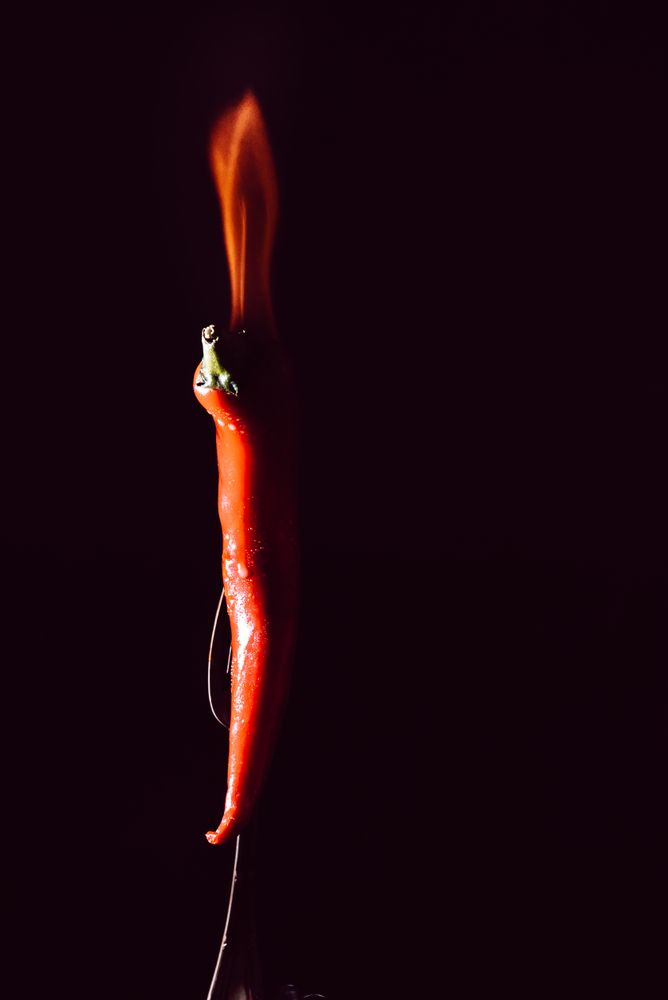 red chili pepper on fire in fork on a dark background
