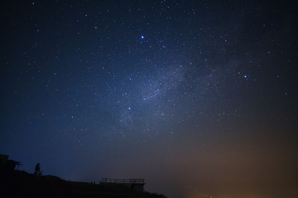Silhouette of a standing man with telescope or camera watching the wilky way galaxy
