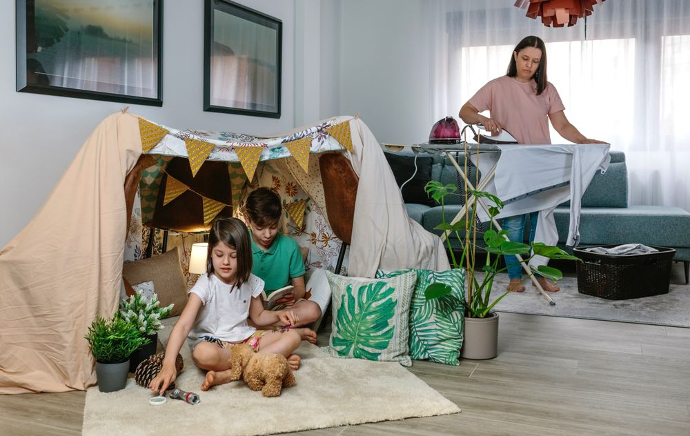 Mother ironing while her children play camping at home